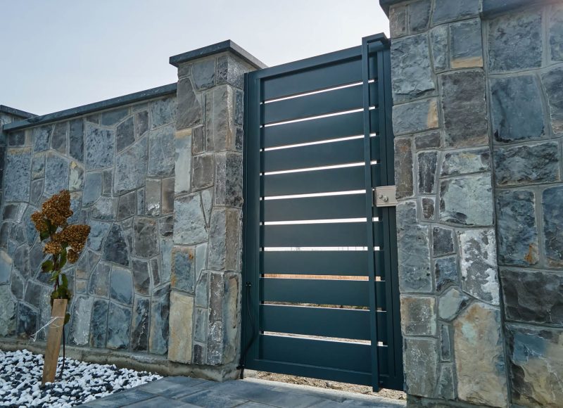 Stone high fence with shut iron door in paved yard of modern style design property outdoor