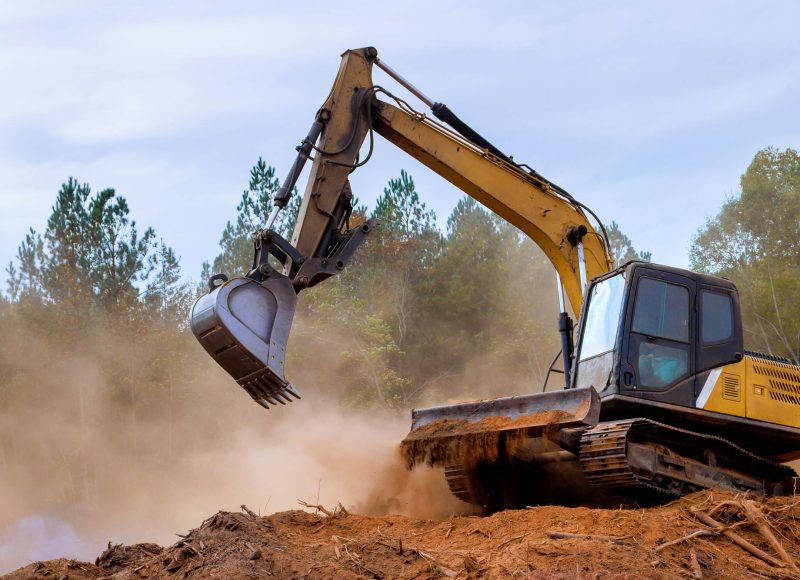 Excavator working on construction site clearing land for development in forested area