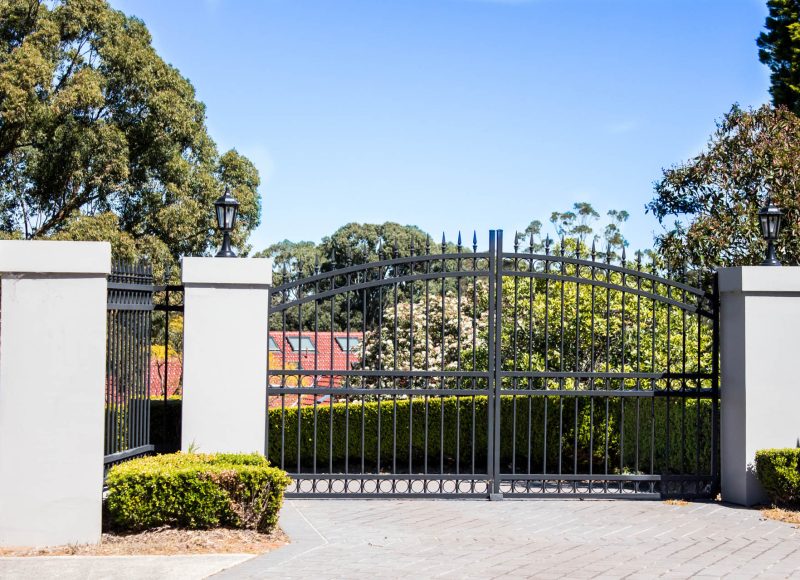 Black metal driveway entrance gates set in brick fence with gard